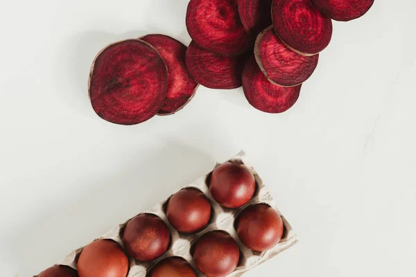 Top view of painted chicken eggs in egg box and beetroot slices on grey — Stock Photo