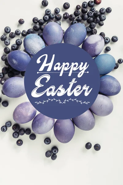 Purple painted chicken eggs, blueberries and happy easter inscription on grey — Stock Photo