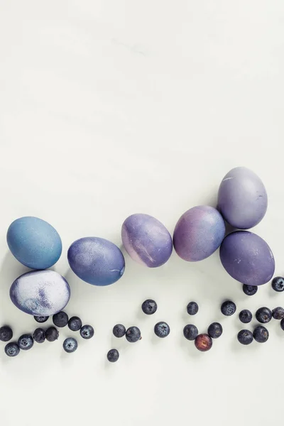 Vue de dessus des oeufs de Pâques violets peints traditionnels et des bleuets sur gris — Photo de stock