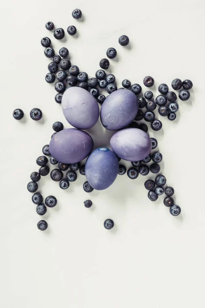 Vue de dessus des œufs de Pâques violets et des bleuets sur gris — Photo de stock