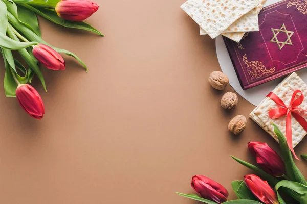 Top view of traditional book with text in hebrew, bouquets of red tulips and matza on table — Stock Photo