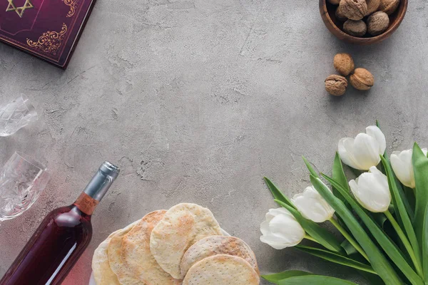 Vista superior del libro tradicional con texto en hebreo, matza y vino sobre mesa de hormigón - foto de stock