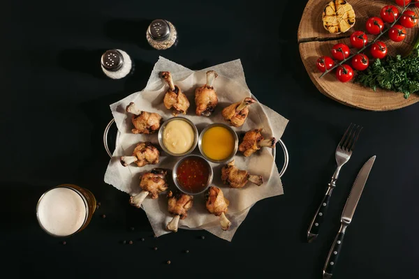 Vista dall'alto del delizioso pollo arrosto con varie salse su carta da forno, spezie, vetro di birra e verdure su nero — Foto stock