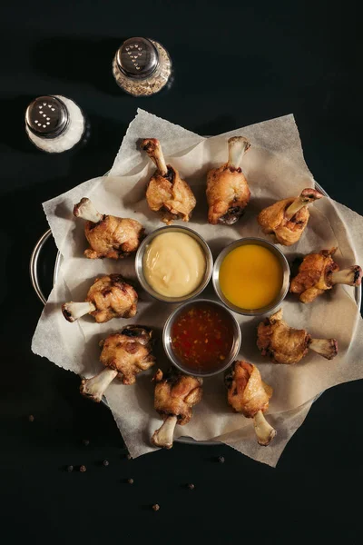 Vista superior de delicioso pollo asado con varias salsas en papel de hornear y especias en negro - foto de stock