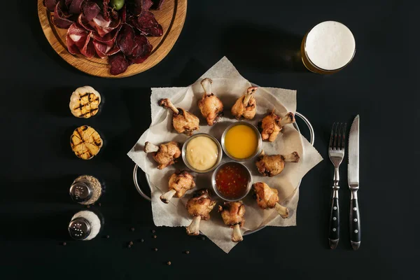 Vista superior de delicioso frango assado com vários molhos em papel manteiga e copo de cerveja em preto — Fotografia de Stock