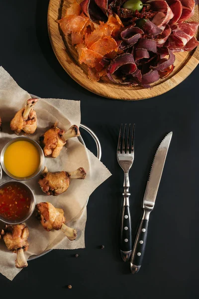 Délicieux poulet rôti avec diverses sauces, viande gastronomique assortie et fourchette avec couteau sur noir — Photo de stock