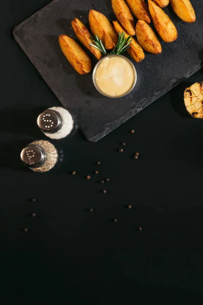 Top view of spices, baked potatoes with sauce and grilled garlic on black — Stock Photo