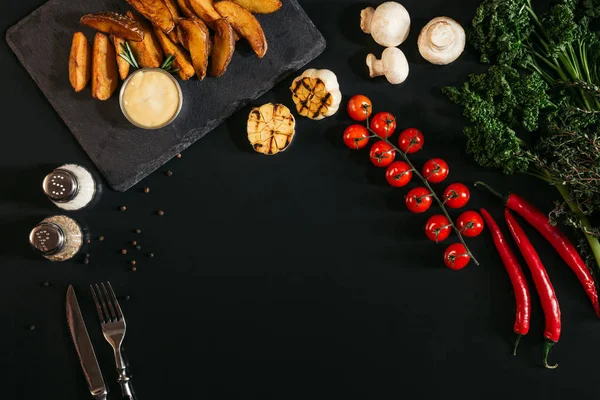 Vista dall'alto di patate al forno saporite con salsa, spezie e verdure su nero — Foto stock