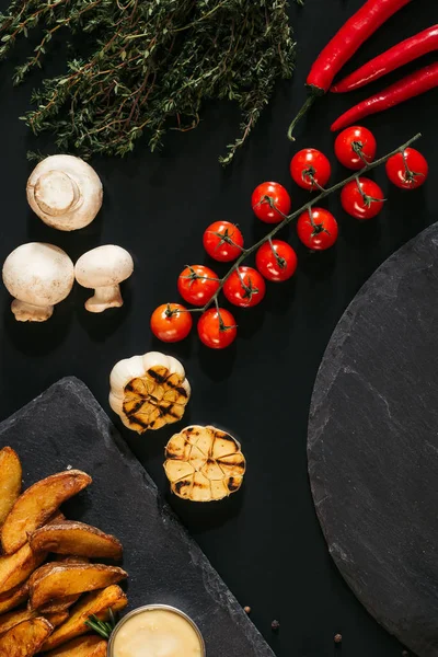 Vista superior de papas al horno, salsa y verduras en negro - foto de stock