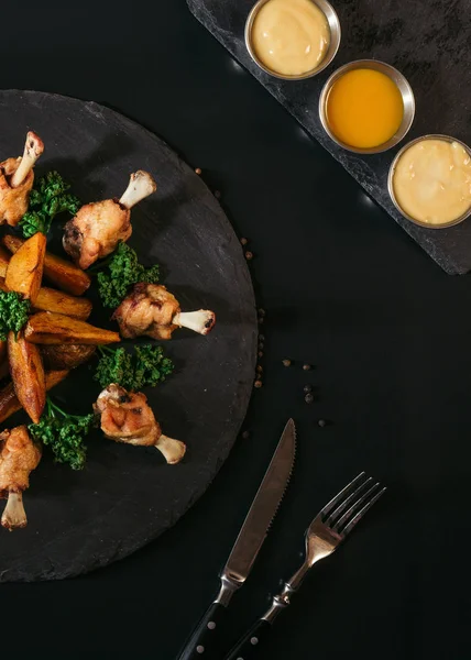 Vista superior de batatas assadas saborosas com frango, vários molhos e garfo com faca em preto — Fotografia de Stock