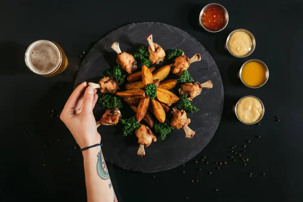 Colpo ritagliato di persona mangiare delizioso pollo arrosto con patate e salse varie sul nero — Foto stock