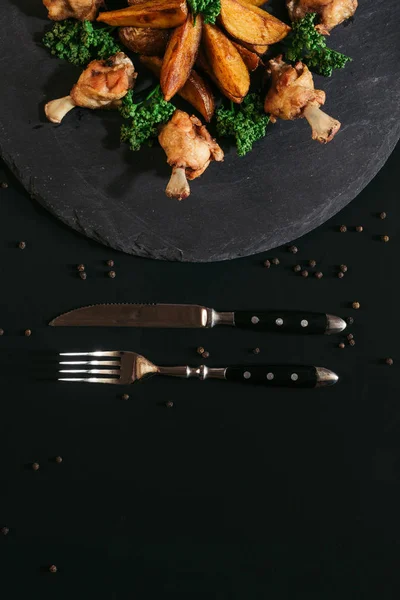 Vista superior de sabrosas patatas asadas con pollo y tenedor con cuchillo sobre negro - foto de stock