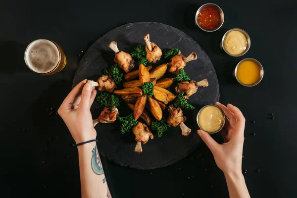 Plan recadré de la personne qui mange de savoureuses pommes de terre au four avec du poulet frit et des sauces sur noir — Photo de stock