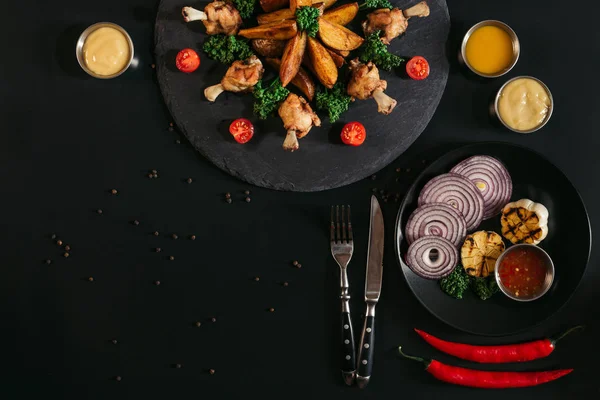 Vue de dessus des pommes de terre rôties savoureuses avec poulet, sauces et légumes sur noir — Photo de stock