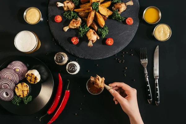 Vista superior parcial de la persona sosteniendo delicioso ala de pollo con salsa en negro - foto de stock