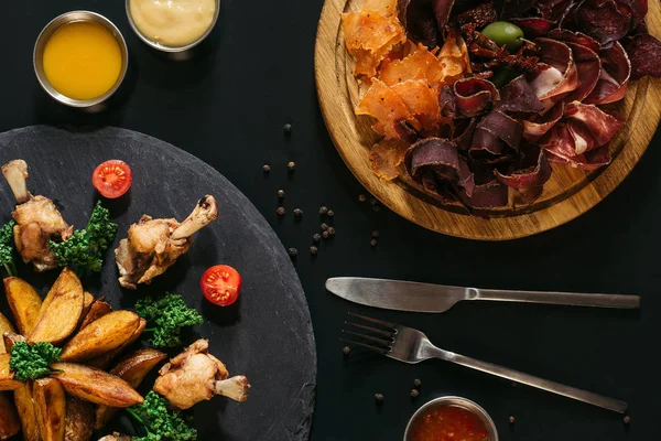 Vue de dessus des pommes de terre rôties savoureuses avec du poulet et de la viande assortie gastronomique sur noir — Photo de stock