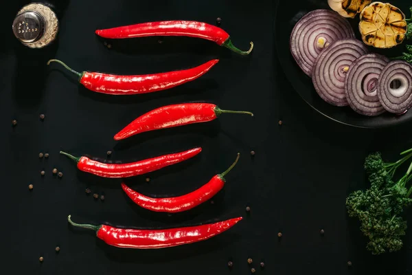 Vista dall'alto di peperoncini rossi, grani di pepe, cipolla affettata e aglio grigliato su nero — Foto stock