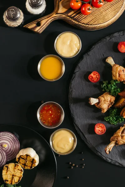 Blick von oben auf leckere gebratene Chicken Wings mit verschiedenen Soßen und Gemüse auf schwarz — Stockfoto