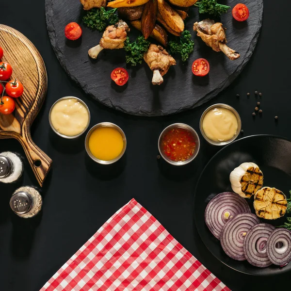 Top view of various sauces, delicious chicken wings and baked potatoes on black — Stock Photo