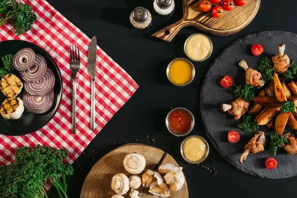 Vista superior de varias salsas, patatas asadas con pollo y verduras en negro - foto de stock