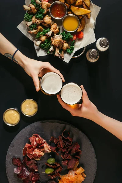 Partial top view of people drinking beer and eating assorted meat and baked potatoes with roasted chicken on black — Stock Photo