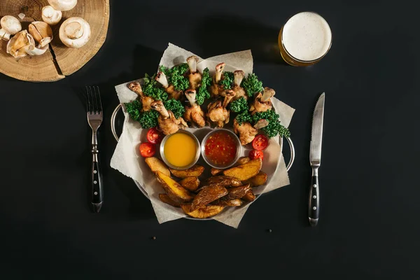 Vista superior de deliciosas papas al horno con pollo asado, salsas y un vaso de cerveza en negro - foto de stock