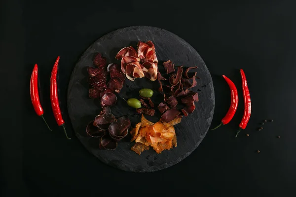 Вид сверху на изысканное разнообразное мясо с оливками на доске и перцем чили на черном — стоковое фото