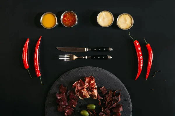 Viande gastronomique assortie sur planche d'ardoise, fourchette avec couteau, diverses sauces et piments noirs — Photo de stock