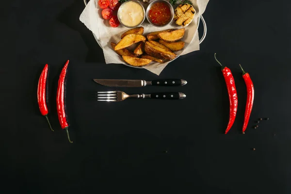 Delicious baked potatoes with sauces, glass of beer, chili peppers and fork with knife on black — Stock Photo