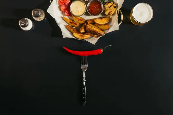 Сверху вид на красный острый перец чили на вилке и вкусный жареный картофель с соусами на черном — стоковое фото