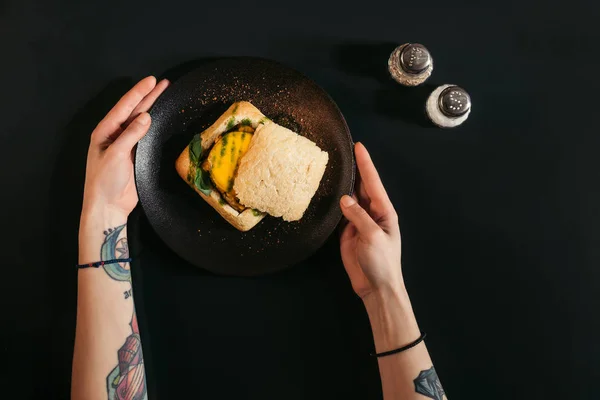 Vista superior parcial de pessoa comendo delicioso hambúrguer vegan no preto — Fotografia de Stock