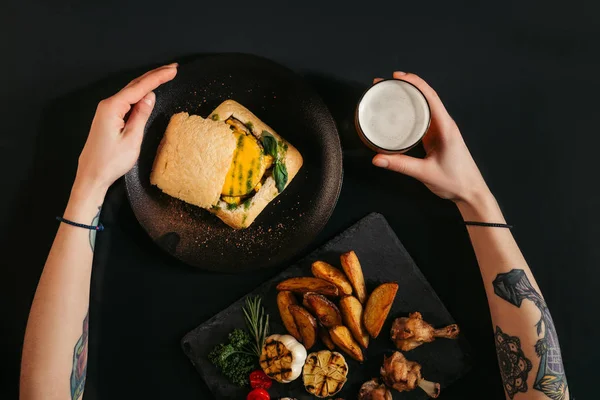 Vue de dessus de la personne manger un délicieux hamburger végétalien avec des pommes de terre frites et boire de la bière sur noir — Photo de stock