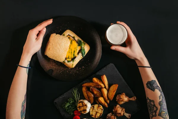 Top view of person eating delicious vegan burger with fried potatoes and drinking beer on black — Stock Photo