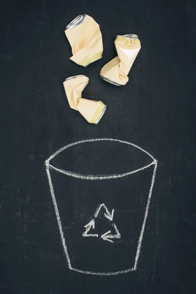 Metal cans falling into drawn trash bin with recycle sign on chalkboard — Stock Photo