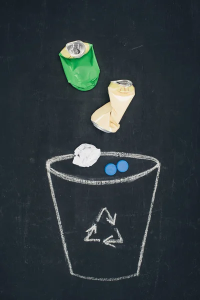 Latas de metal con papel arrugado cayendo en cubo de basura dibujado con cartel de reciclaje en pizarra — Stock Photo