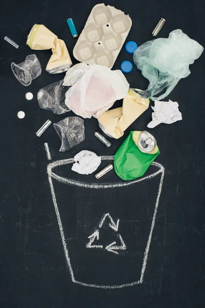 Various types of trash falling into drawn trash bin with recycle sign on chalkboard — Stock Photo