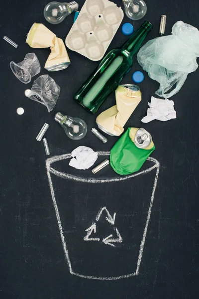 Various types of trash falling into drawn trash can with recycle sign on chalkboard — Stock Photo