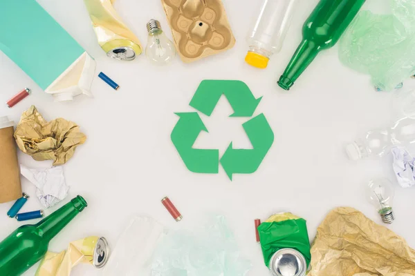 Top view of various types of trash surrounding recycle sign on white — Stock Photo