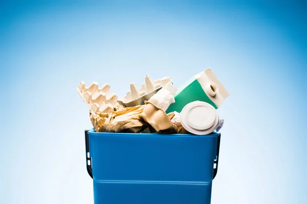 Various paper trash in trash bin on blue — Stock Photo