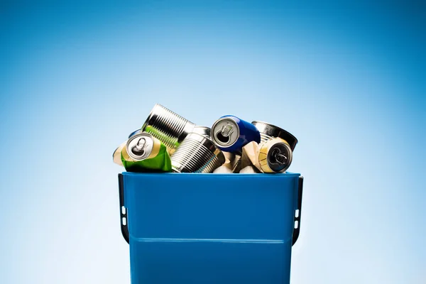 Various metal cans in trash bin on blue — Stock Photo