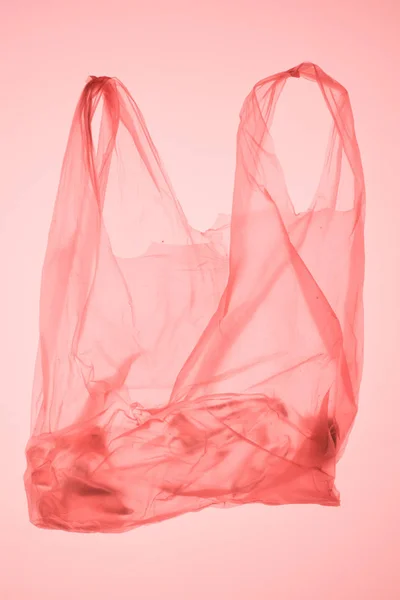 Crumpled plastic bag with bottle inside under pastel pink toned light — Stock Photo