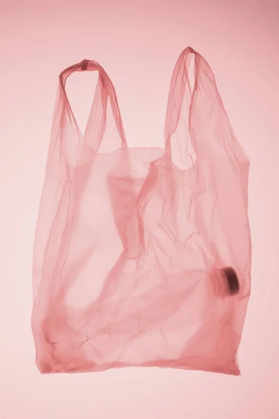 Transparent plastic bag with bottle inside under pastel pink toned light — Stock Photo
