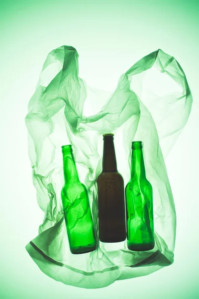 Saco de plástico transparente com garrafas de vidro sob luz verde tonificada — Fotografia de Stock