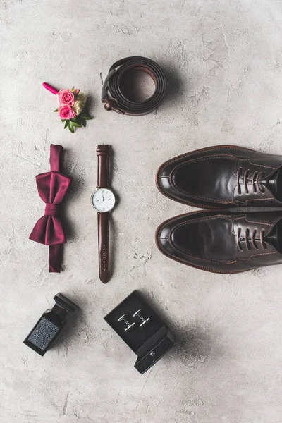 Vista superior de corbata de lazo, boutonniere, reloj de pulsera y zapatos para boda en superficie gris - foto de stock