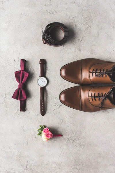 Vista superior de la corbata de lazo de boda, boutonniere, reloj de pulsera y zapatos para el novio en la superficie gris - foto de stock