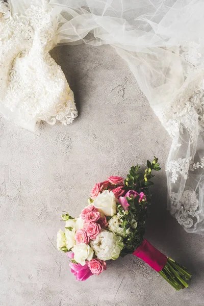 Vista dall'alto di abito da sposa e bouquet su superficie grigia — Foto stock