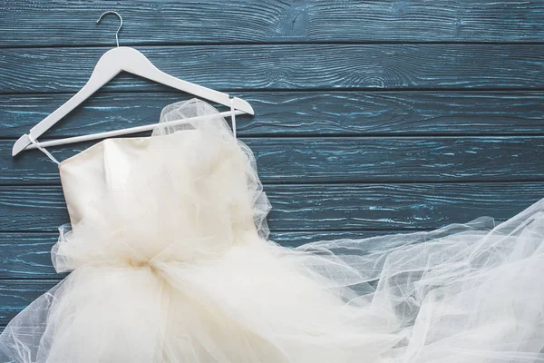 Vista dall'alto di abito da sposa bianco su appendino su tavolo in legno blu scuro — Foto stock