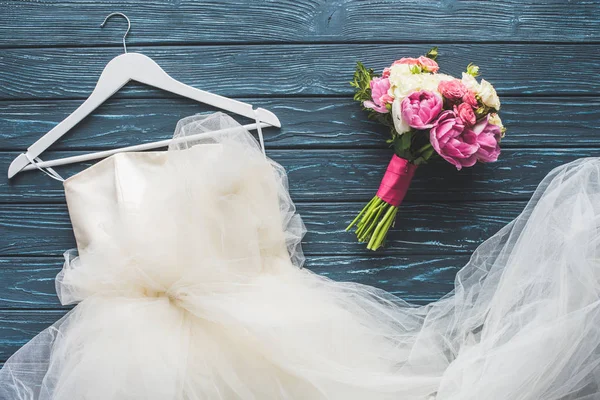 Верхний вид свадебного букета и белого платья на деревянный темно-синий стол — стоковое фото