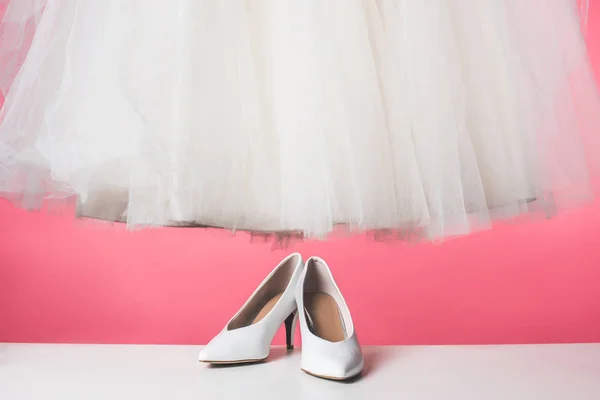 Par de zapatos blancos y vestido de novia aislado en rosa - foto de stock