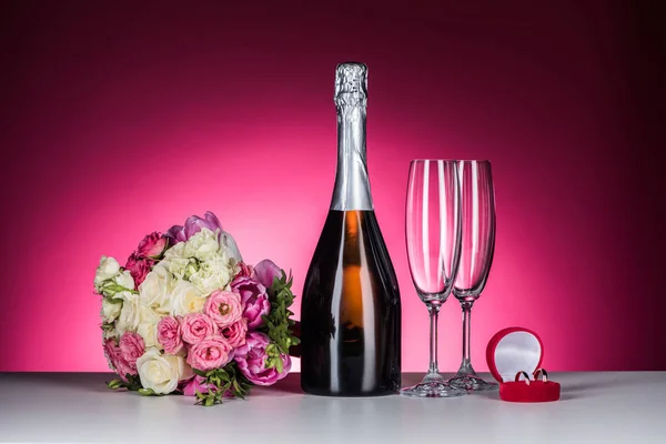 Buquê de casamento, anéis de casamento e champanhe na mesa em rosa — Fotografia de Stock